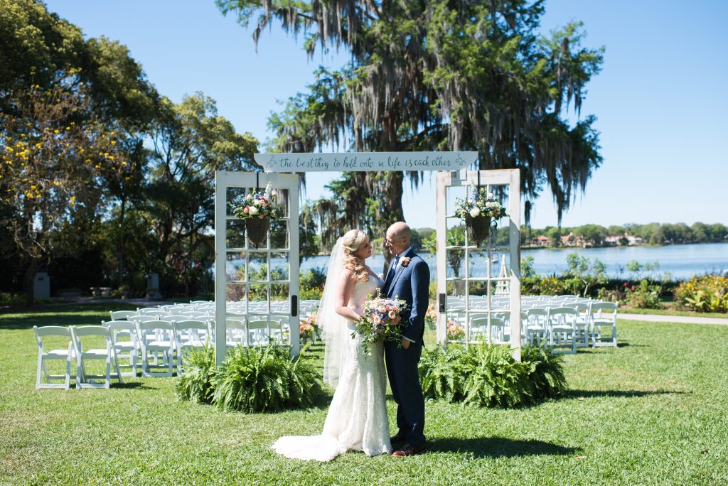bride and groom pose on wedding day in front of ceremony location on the lake