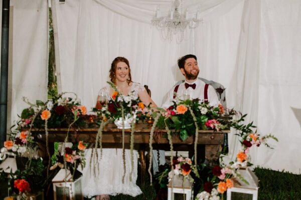 bride and groom sit at sweetheart table on wedding day planned by anna christine events in orlando wedding
